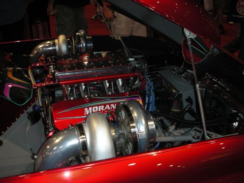 1998 Ford Crown Victoria - twin-turbocharged engine with a 'Moran' billet intake and large chrome turbos sits under the open hood of a red car.