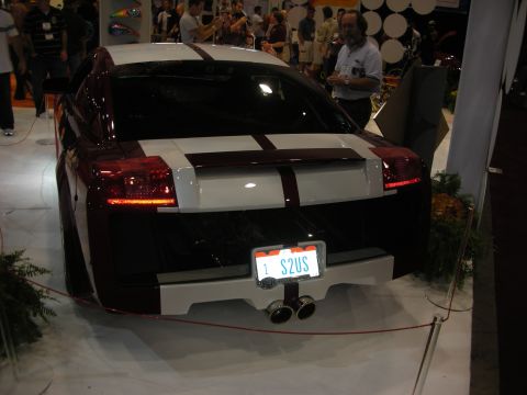 1998 Ford Crown Victoria - Rear view of a dark Lamborghini coupe with white twin stripes, an 'S2US' plate and quad center-exit exhaust on a show floor.