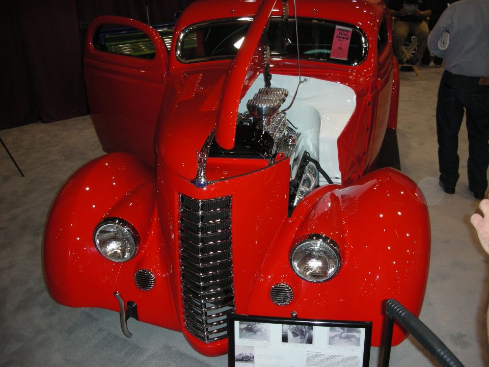 Bright red 1930s-style hot rod coupe with chrome grille and dual headlights