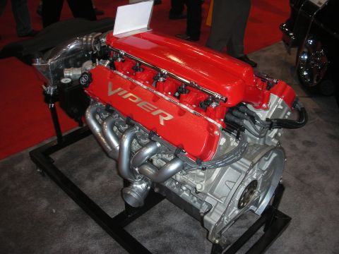 1998 Ford Crown Victoria - red Dodge 'Viper' V10 engine sits on a display stand showing its exhaust headers and bare aluminum block.