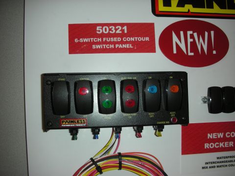 1998 Ford Crown Victoria - Painless Performance '50321' six-switch fused rocker panel with lit colored switches displayed against marketing signage.