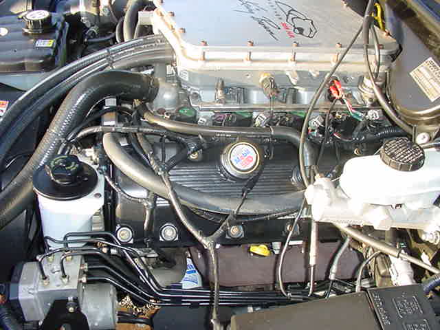 Engine bay with Mobil 1 oil cap, silver intake plenum with cat logo, hoses, brake reservoir and ABS lines