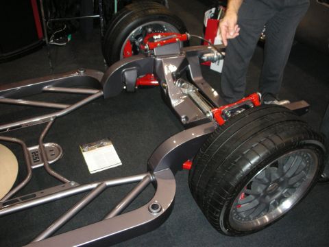 1998 Ford Crown Victoria - fabricated tubular frame with bright red control arms and shock mounts holds a mounted tire on dark show carpeting.