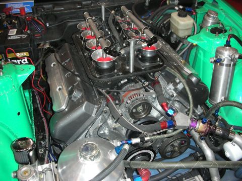 1998 Ford Crown Victoria - Close-up of a V8 fitted with individual throttle-body velocity stacks, fuel rails and braided AN lines inside a green engine bay.