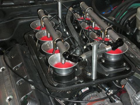 1998 Ford Crown Victoria - Detailed view of red-anodized velocity stacks set in a carbon-fiber tray, fed by polished steel fuel rails on a race engine.