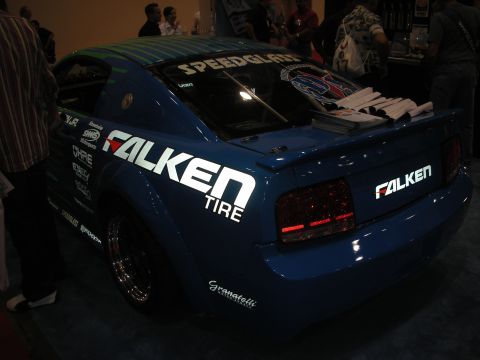 1998 Ford Crown Victoria - blue late-model Mustang coupe in Falken Tire and Speedglas livery sits on display rear-three-quarter at an indoor trade show.