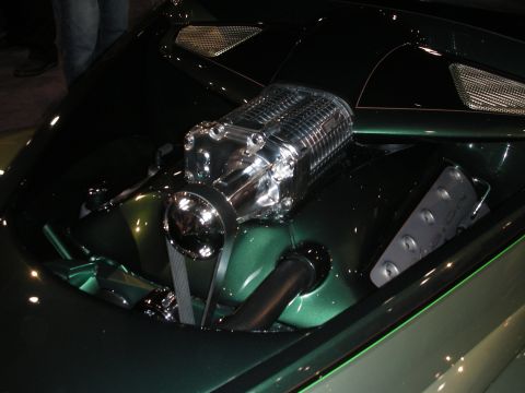 1998 Ford Crown Victoria - large polished twin-screw supercharger sits atop an engine recessed in a glossy green custom body under show lighting.