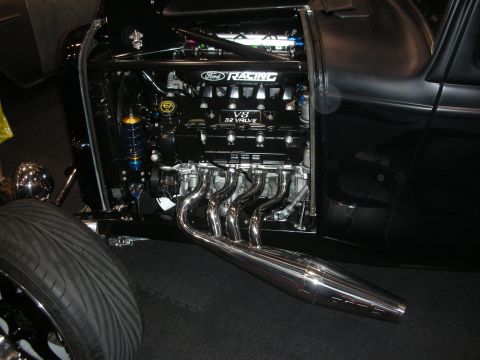 1998 Ford Crown Victoria - black hot rod displays an exposed Ford Racing 32-valve V8 with chrome side-exit headers and a coilover shock.