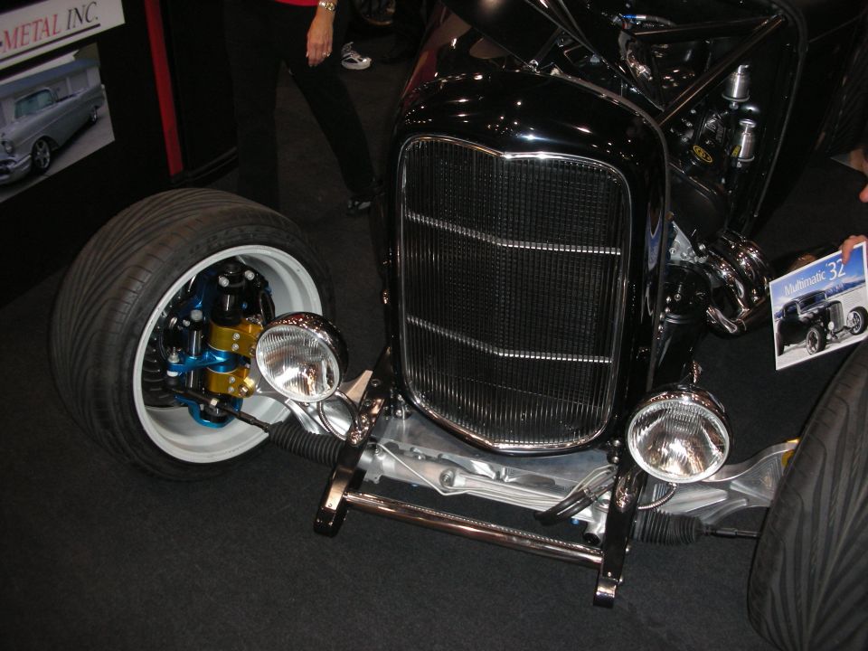Front of a black hot rod with chrome grille, white tire and exposed brake