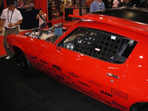 1998 Ford Crown Victoria - red Camaro shows an exposed supercharged engine and a black window safety net, its door covered in sponsor decals.