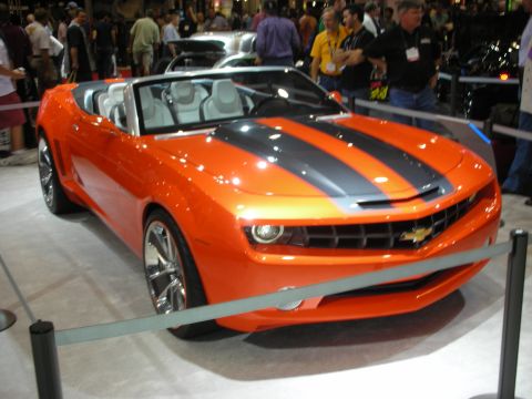 1998 Ford Crown Victoria - orange Chevrolet Camaro convertible with black racing stripes and gray interior sits roped off on a crowded show floor.