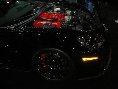 1998 Ford Crown Victoria - black sports car displayed at an indoor show, its red-finned engine visible beneath a clear cover above a black multi-spoke wheel with a re…