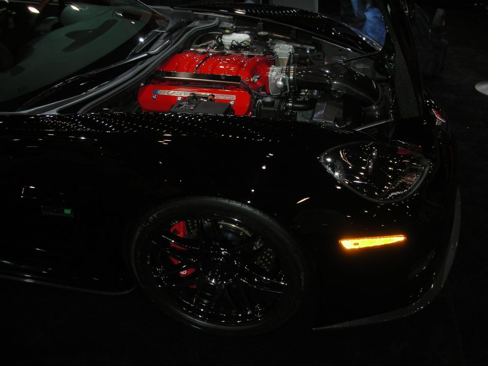Black sports car at show with red engine visible through clear engine cover and black wheel with red brake caliper