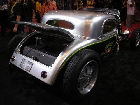 1998 Ford Crown Victoria - Rear three-quarter view of a bare-metal silver custom hot rod coupe with an open trunk, green pinstriping, and a high rear wing at an indoo…
