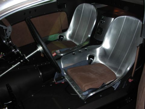 1998 Ford Crown Victoria - Twin bare aluminum bucket seats with brown suede cushions inside a stripped custom hot rod interior beside a black steering wheel.