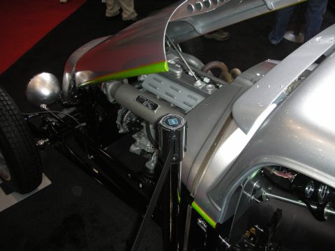1998 Ford Crown Victoria - engine bay of a bare-metal silver hot rod with a finned cast intake cover and a louvered side panel, displayed at an indoor show.