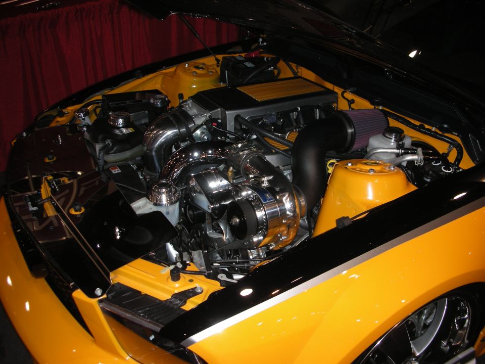 Chrome supercharged engine in the bay of a yellow car with K&N cone filter at a show