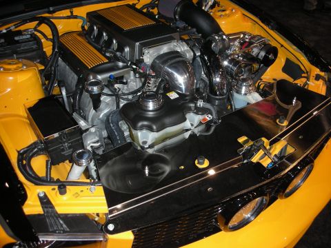 1998 Ford Crown Victoria - detailed engine bay of a yellow car showing finned valve covers, a polished supercharger, and a smoothed black inner fender.