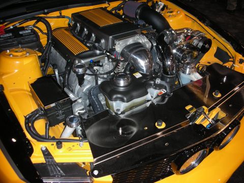 1998 Ford Crown Victoria - second view of a yellow car's engine bay featuring finned cam covers, a chrome supercharger, and tidy smoothed black panels.