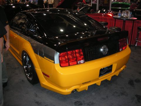 1998 Ford Crown Victoria - Rear three-quarter view of a yellow-and-black Ford Mustang coupe with a wide body kit and Procharger graphics on a show floor.