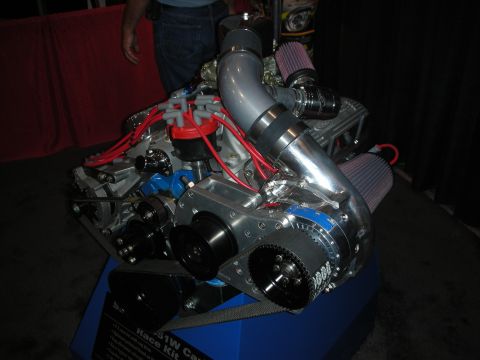 1998 Ford Crown Victoria - polished crate V8 engine fitted with twin red cone air filters and red spark-plug wires sits on a display stand at a show.