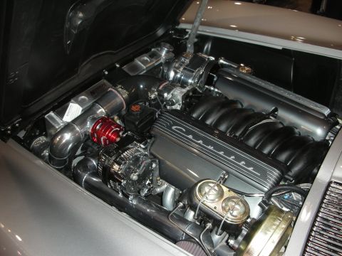 1998 Ford Crown Victoria - engine bay of a silver Chevrolet Corvette showing a fuel-injected V8 with a black cam cover scripted Corvette and polished plumbing.