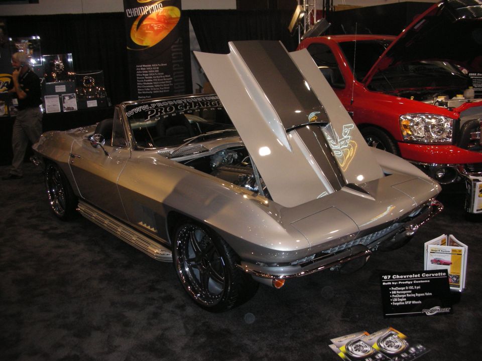Silver mid-1960s Chevrolet Corvette convertible with open hood at an indoor show stand