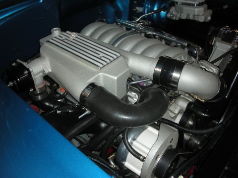 1998 Ford Crown Victoria - silver Roots-style supercharger sits atop a V8 engine with a black intake coupler inside a teal-blue painted engine bay.