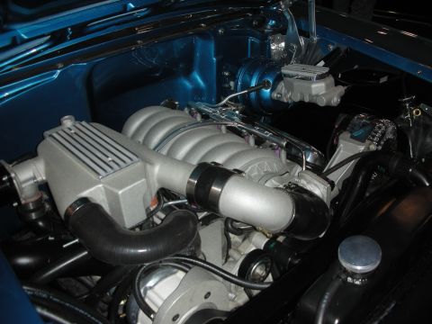 1998 Ford Crown Victoria - supercharged V8 with a finned silver blower case and chrome valve covers mounted in a teal-blue painted engine bay.