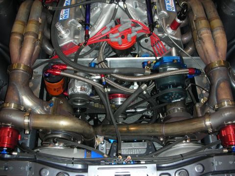 1998 Ford Crown Victoria - densely packed twin-turbo V8 engine bay showing swept stainless headers, braided steel lines and numerous red anodized fittings.