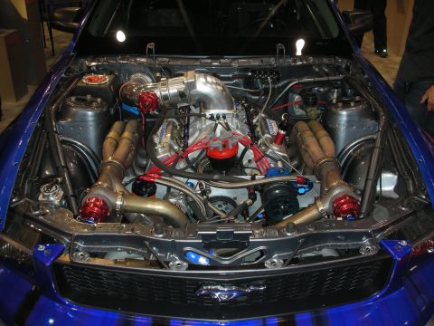 1998 Ford Crown Victoria - twin-turbo engine bay of a blue Ford Mustang, with two large turbos, gold heat-coated headers, and red spark-plug wires.