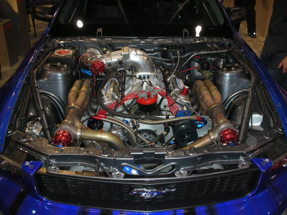 Twin-turbo engine bay of a blue Ford Mustang with chrome turbos and red plug wires