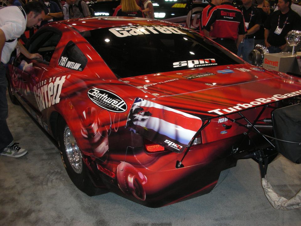 Rear of a red Garrett-liveried turbo drag car with airbrushed graphics and parachute mount at a show