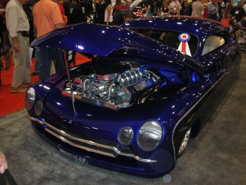 1998 Ford Crown Victoria - purple chopped lead-sled custom car with its hood open revealing a chrome blown V8, wearing a Mercules nose badge at a show.