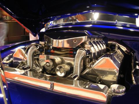 1998 Ford Crown Victoria - Highly polished engine bay of a deep blue custom car, with chrome valve covers, braided stainless lines and orange accents.