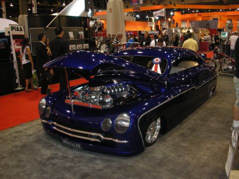 1998 Ford Crown Victoria - Lowered, chopped deep-blue custom coupe with hood open showing a chromed engine, displayed on red carpet at an indoor show.