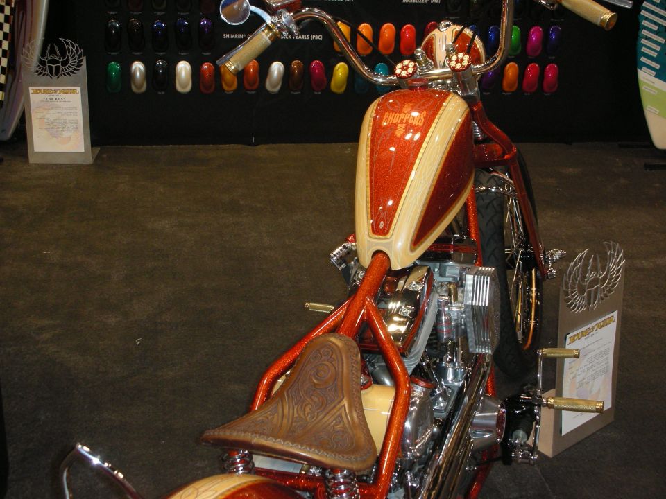 Custom chopper motorcycle with orange metalflake tank and tooled-leather seat at a show