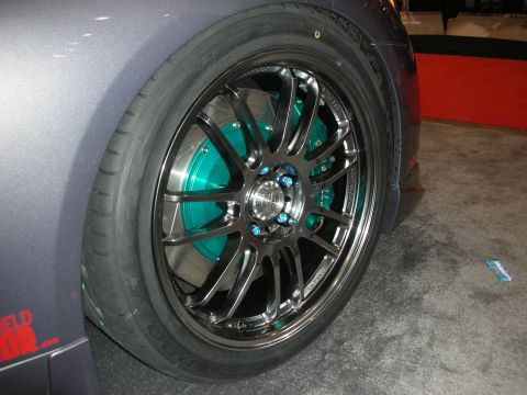 1998 Ford Crown Victoria - Close-up of a gunmetal multi-spoke alloy wheel on a low-profile tire, with a teal-painted brake rotor and blue lug nuts.
