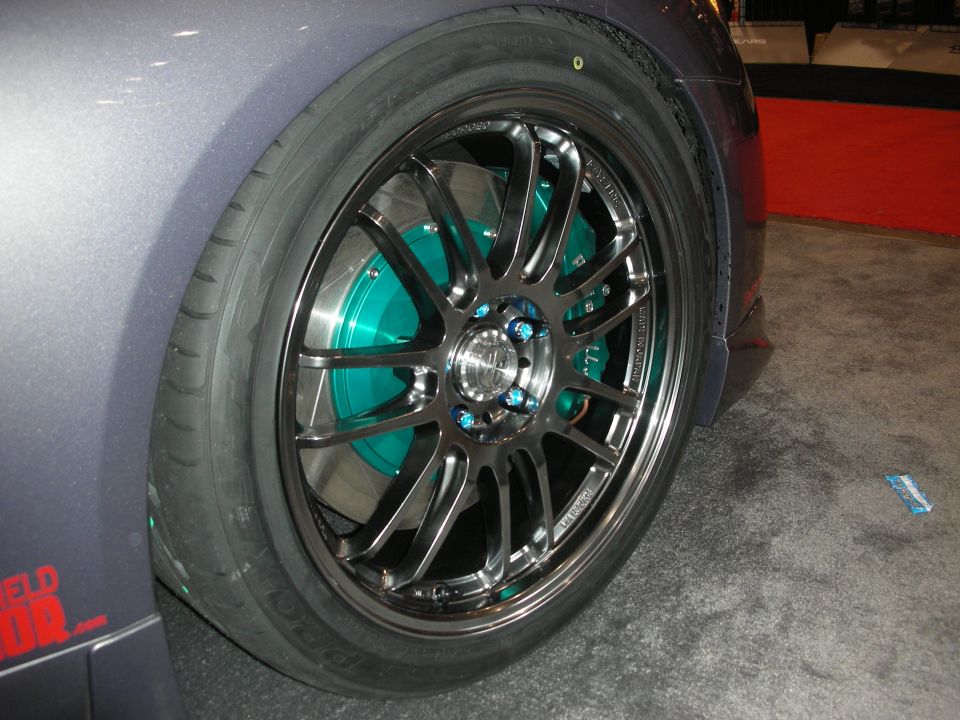 Close-up of a gunmetal multi-spoke wheel with teal-painted brake caliper and rotor
