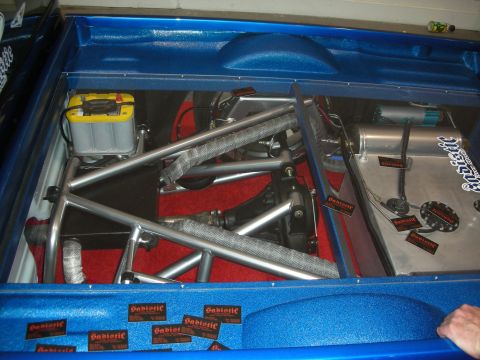 1998 Ford Crown Victoria - Custom blue trunk compartment revealing tubular chassis bracing, a battery and red carpet, lined with sponsor decals.