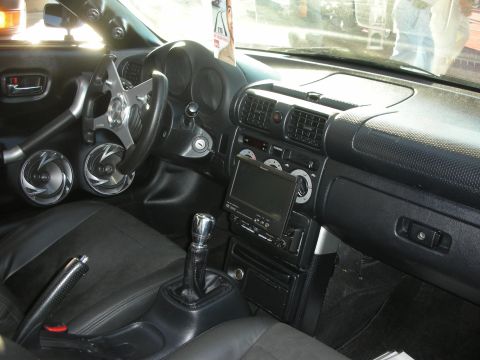 1998 Ford Crown Victoria - Black leather sport-car interior showing a three-spoke steering wheel, manual shifter, gauges and an in-dash touchscreen.