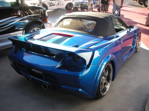 1998 Ford Crown Victoria - Rear of a blue widebody Toyota MR2 Spyder showing a vented engine cover, ducktail spoiler and stacked dual exhausts.