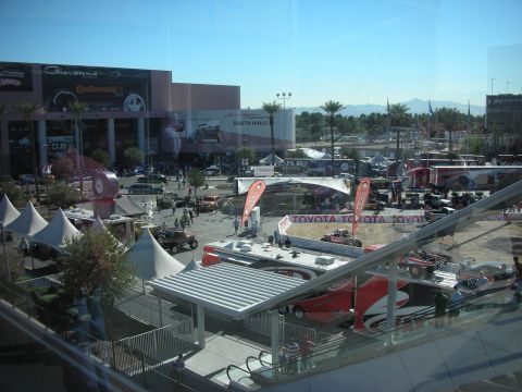 1998 Ford Crown Victoria - View through tinted glass over an outdoor show plaza with white tents, Toyota banners and parked vehicles near a hall.