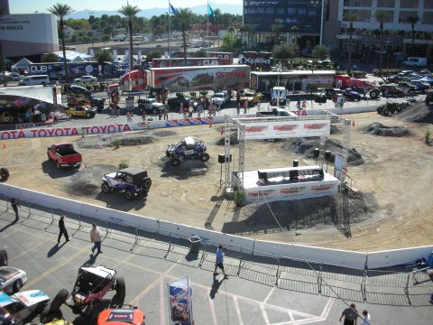 1998 Ford Crown Victoria - Aerial view of a fenced dirt off-road course ringed with Toyota banners, with off-road vehicles and a media booth.