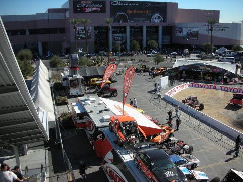 1998 Ford Crown Victoria - Elevated view of a show plaza with parked race cars, orange banners and tents in front of a large convention hall.
