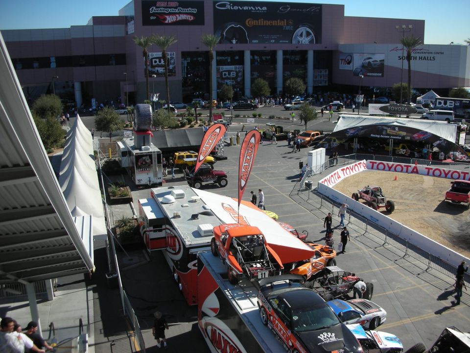 Elevated view of a show plaza with race cars, tents and a convention hall facade