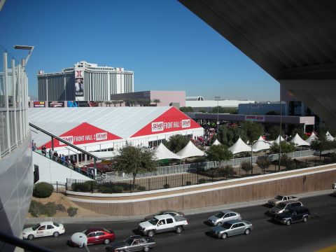 1998 Ford Crown Victoria - View across a road toward large red-and-white SEMA event tents, with passing cars and hotel towers in the background.