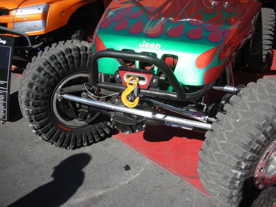 Front suspension and winch of a green-and-red flamed Jeep rock crawler with mud tires