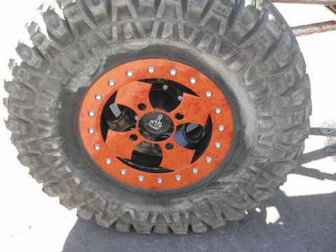 1998 Ford Crown Victoria - Close-up of an aggressive off-road mud tire mounted on a black-and-orange beadlock wheel with a skull center cap.