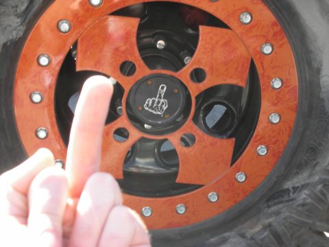 1998 Ford Crown Victoria - finger points at a black wheel center cap showing a middle-finger emblem, set in an orange-and-black beadlock rim on an off-road tire.